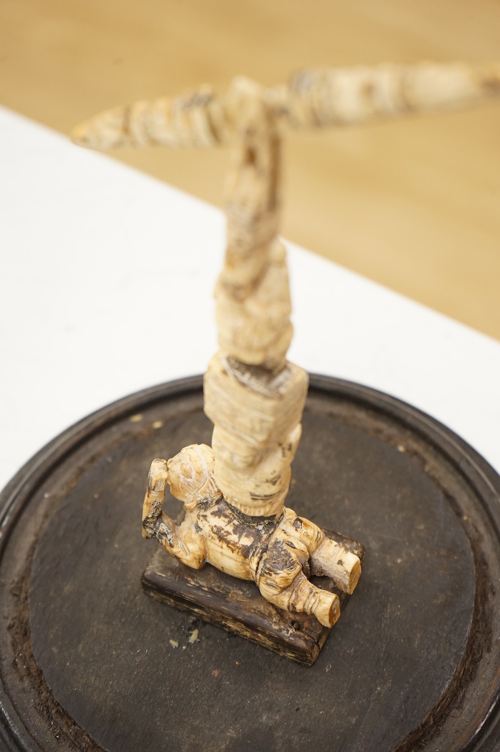A 19th century Indian bone sculptural devotional object, carved as a totem with Ganesh and other deities, pivoting beam, 18cm high, glass dome with ebonised base